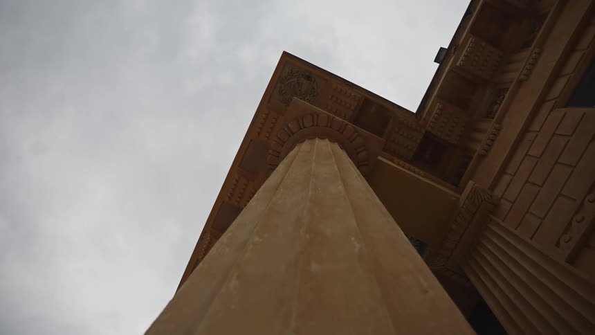 A low-angle view looks up a grand, fluted architectural column towards the overcast sky