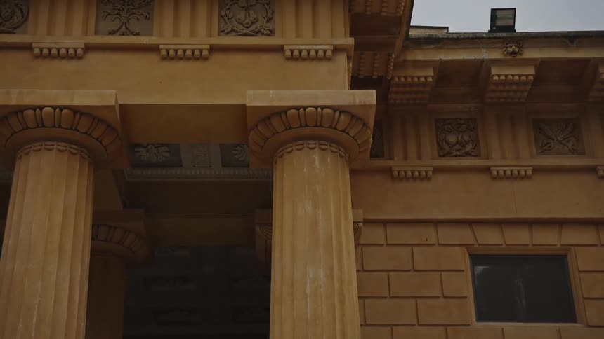 A static close-up shot of the ornate columns and frieze on a neoclassical building against an overcast sky