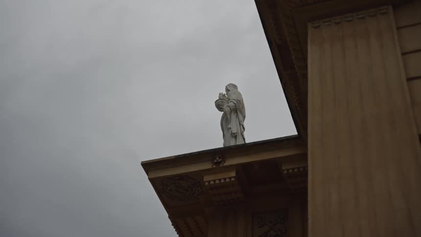 A low-angle view of a solitary white statue on a building's roof under a somber, overcast sky