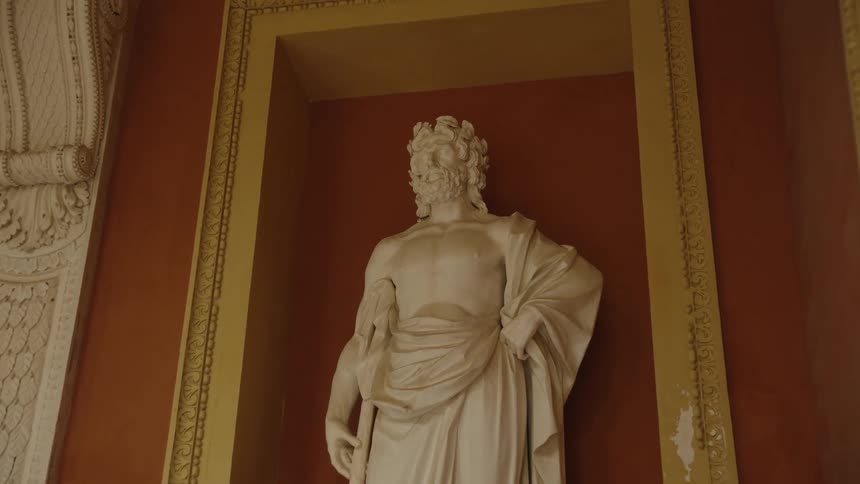 A slow push-in shot of a classic white marble statue of a Roman god standing in a recessed wall alcove