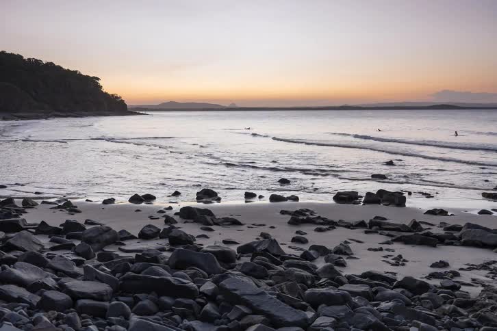 Timelapse of a vibrant sunset over a rocky beach as surfers and people enjoy the last light of the day