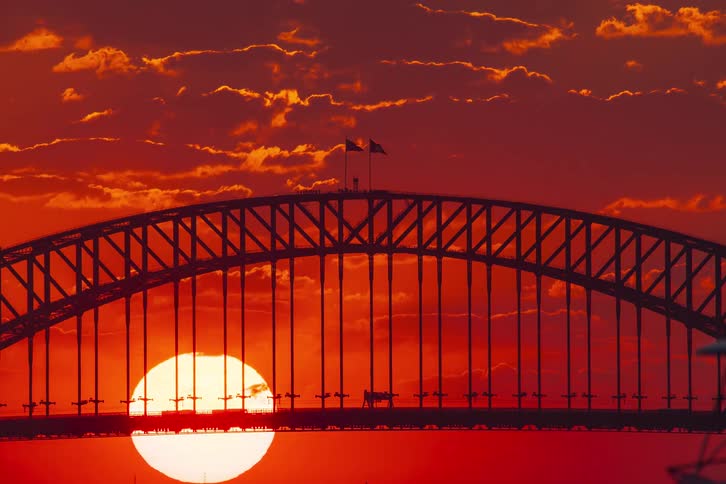 The sun sinks behind the silhouetted Sydney Harbour Bridge in a dramatic, fiery red sunset time-lapse