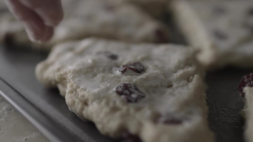 A woman sprinkles sugar onto dough on a cookie sheet