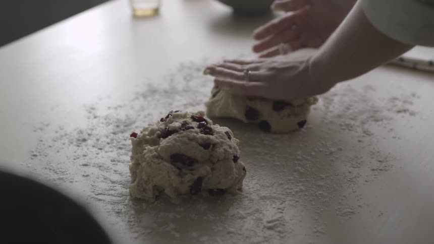 A woman is using her hands to form large balls of dough