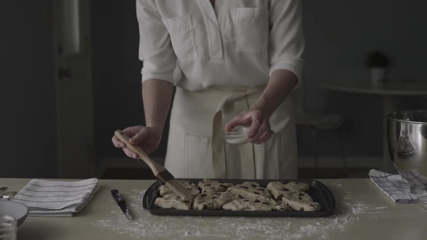 Woman brushes melted butter onto raw cookie dough