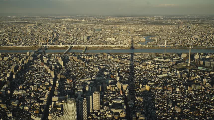 Static wide aerial shot captures the sprawling metropolis of Tokyo, with the distinct shadow of the Skytree tower cast over the city