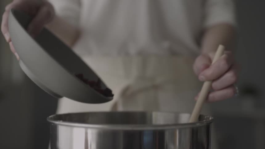 A woman adds ingredients into a cooking pot