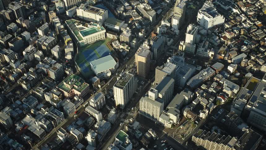 An aerial top-down static view of a dense urban city in Japan as shadows stretch across buildings in the late afternoon