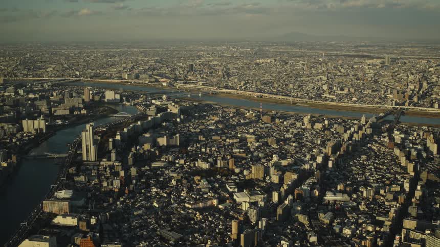 An expansive aerial view captures the vast, dense cityscape of Tokyo, Japan, with a river flowing through it as far as the eye can see