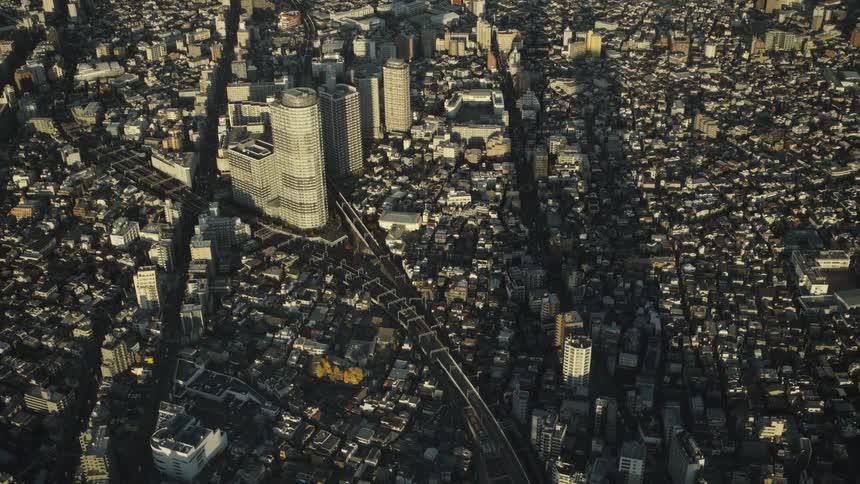 High-angle static aerial view of the dense Tokyo cityscape at golden hour, with trains moving along the tracks through the urban sprawl