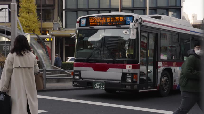 Pedestrians cross a busy city street in slow motion as a public bus and scooter wait at the crosswalk in Japan