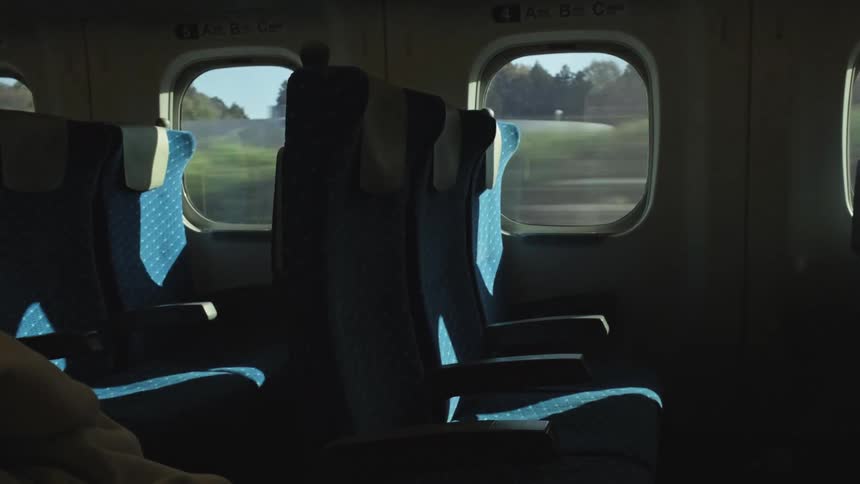 Sunlight illuminates empty seats on a high-speed train as the lush green Japanese countryside speeds by the window