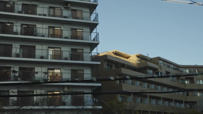 Passing by modern glass skyscrapers and residential apartment buildings on a sunny day in a Japanese city, as seen from a moving train
