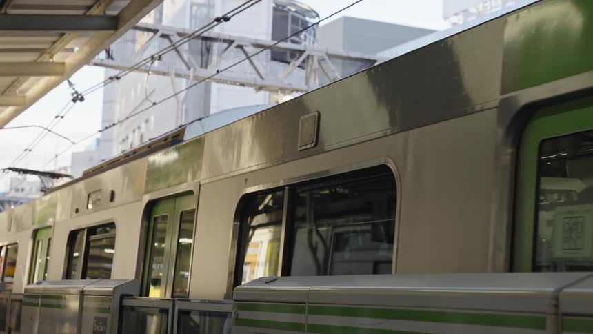 A sleek silver and green Japanese commuter train glides smoothly along the platform at a busy Tokyo station