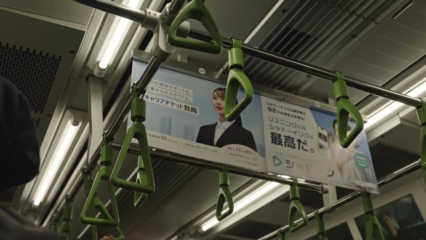 A view of the green hanging hand straps and a Japanese advertisement inside a moving subway train