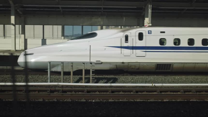 Japanese bullet train, the Shinkansen, departs from a station, viewed from a parallel moving train