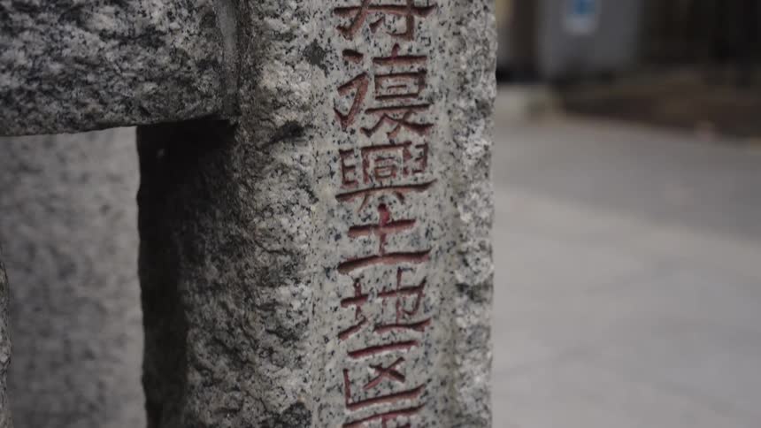 A slow tilt down a weathered granite pillar reveals red Japanese kanji characters carved at the entrance of a traditional temple