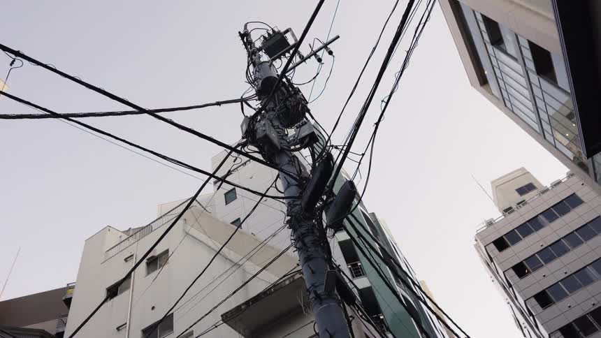 Looking up at a tangled web of electrical power lines on a utility pole in the streets of Tokyo, Japan