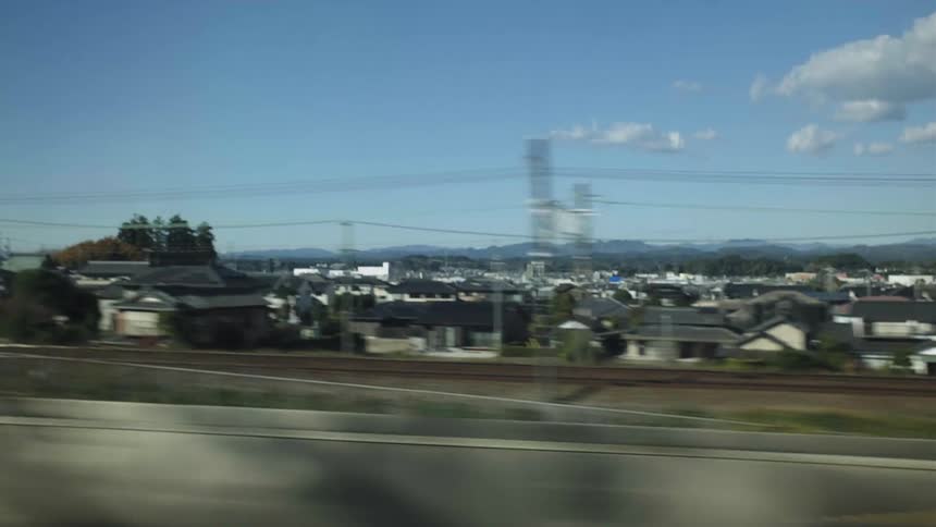Tracking shot from a train window reveals the suburban landscape of a Japanese town under a clear blue sky
