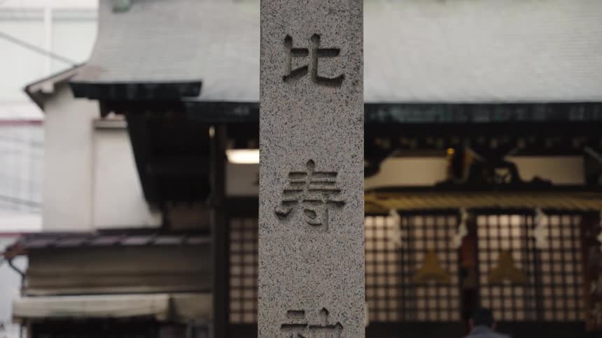 A slow vertical tilt shot reveals Japanese Kanji characters carved into a stone pillar at a traditional shrine in Japan