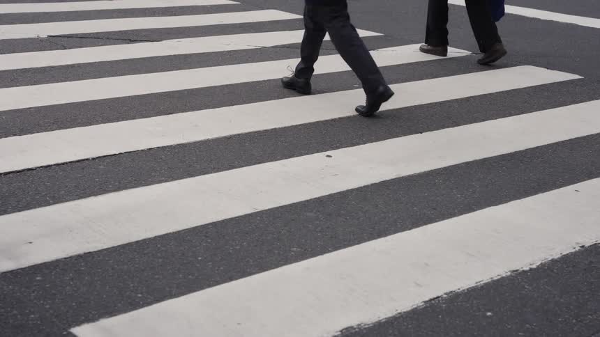 Slow motion shot of the feet of two business people walking across a city street crosswalk
