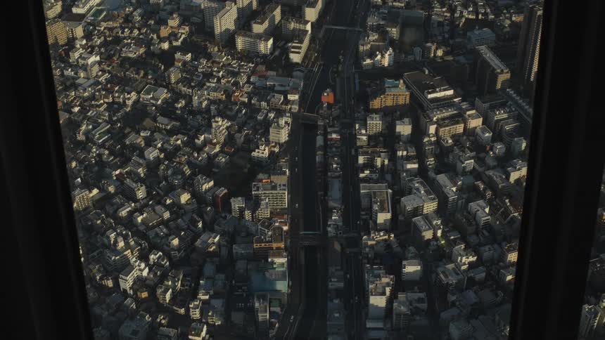 A static aerial view from a window captures the endless sprawl of buildings and a busy highway in a major city