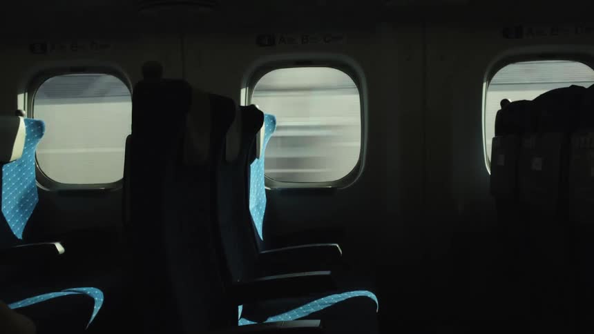 Sunlight illuminates empty blue seats inside a high-speed train as the city scenery rushes past the windows