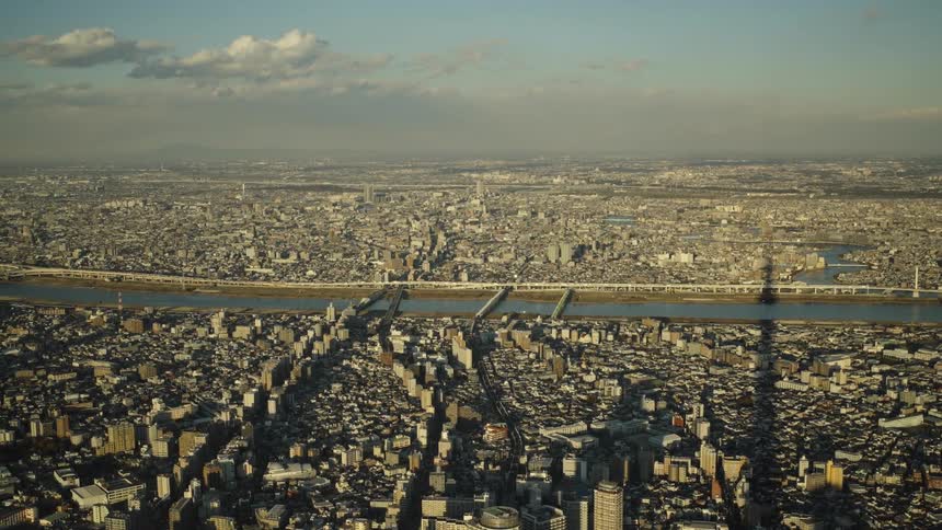 Golden hour aerial shot over the sprawling cityscape of Tokyo, Japan, featuring the river and the long shadow of the Skytree