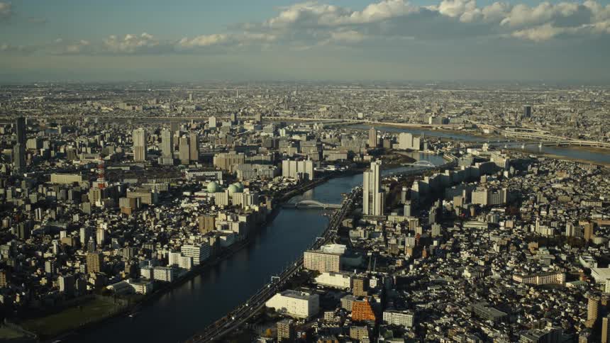 A stunning high-angle, wide shot of Tokyo's dense cityscape showing the Sumida River winding through the sprawling urban metropolis