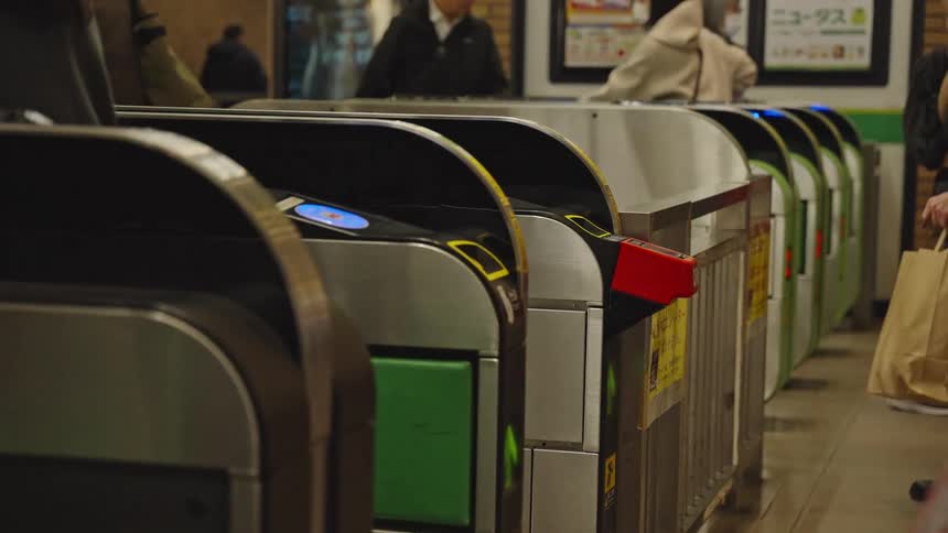 Commuters in Japan tap their fare cards and phones to pass through the electronic turnstiles at a busy train station