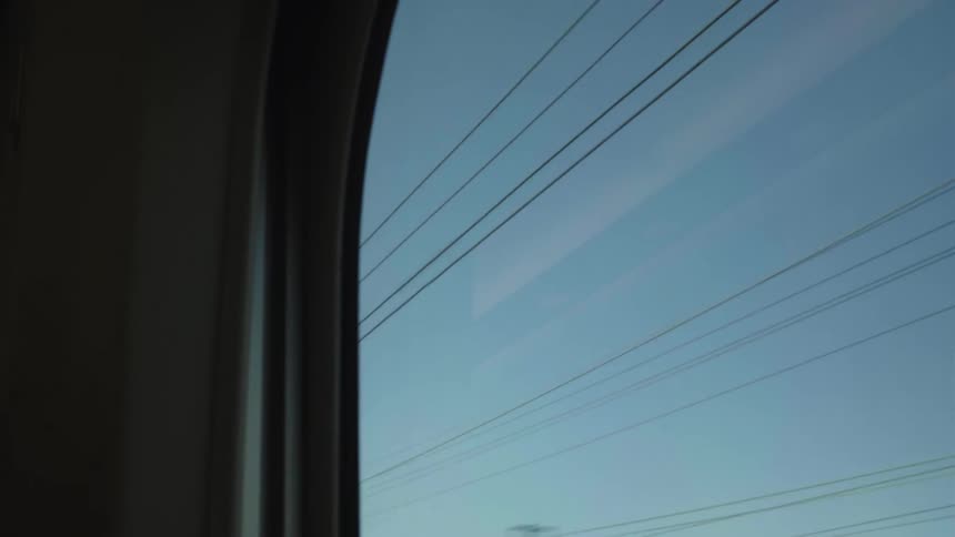 View from a fast-moving train window showing blurred power lines against a clear blue sky