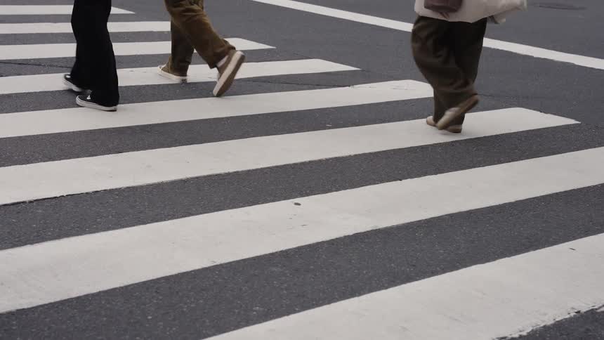 A slow-motion, low-angle view of anonymous pedestrians' feet walking across a city crosswalk