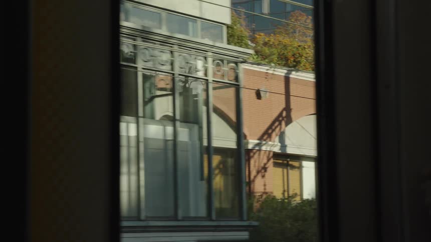 A passenger's perspective of urban architecture passing by from a moving train on a bright, sunny day