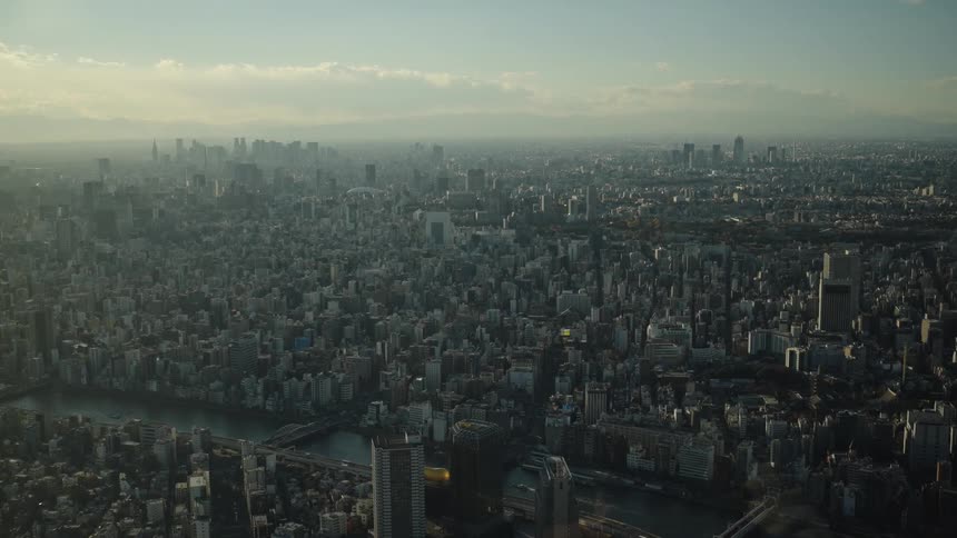 A vast and sprawling aerial view of the Tokyo cityscape under a hazy afternoon sun