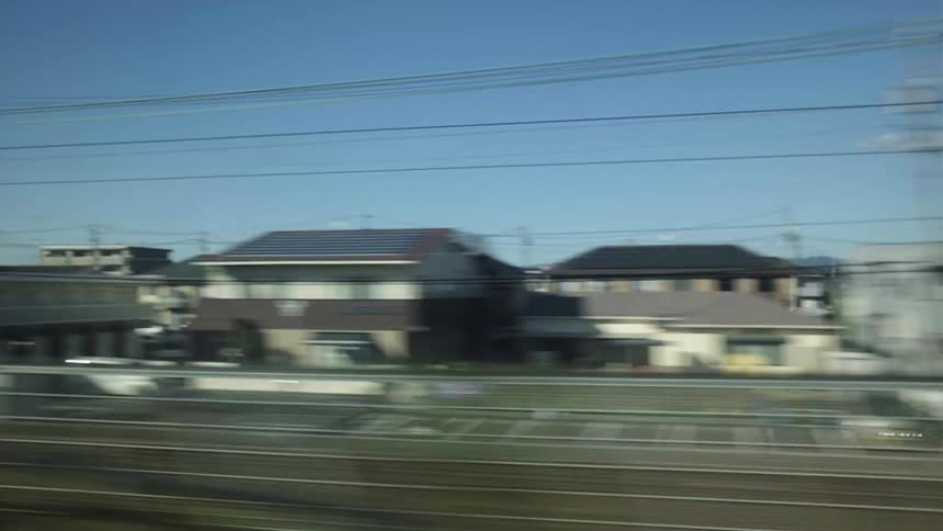 A scenic view of suburban and rural Japanese landscapes with houses and fields passing by from a high-speed train window on a sunny day