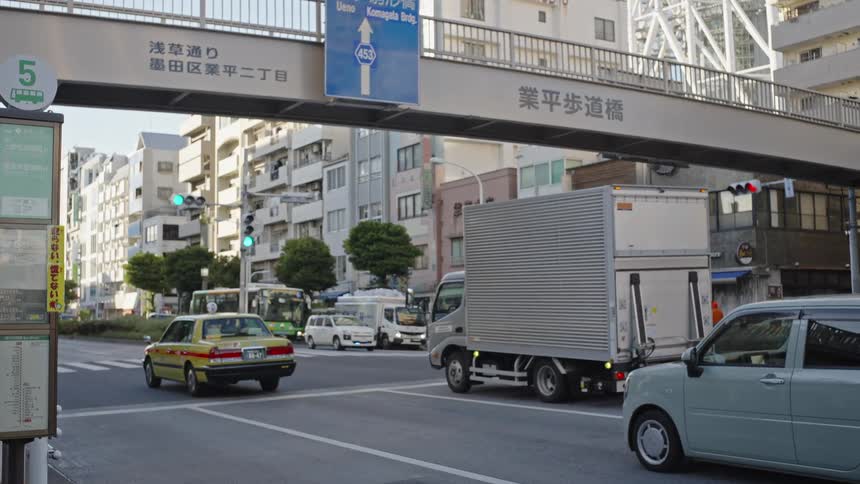Traffic including a yellow taxi cab and a light green car drive through an intersection in Tokyo, Japan