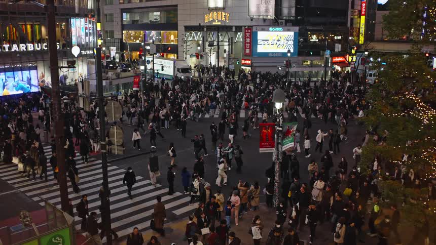 An elevated view captures the organized chaos of pedestrians at the bustling Shibuya Crossing in Tokyo at night