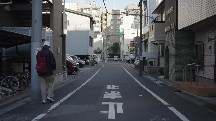 A man with a red backpack walks down a quiet residential street in Tokyo, Japan