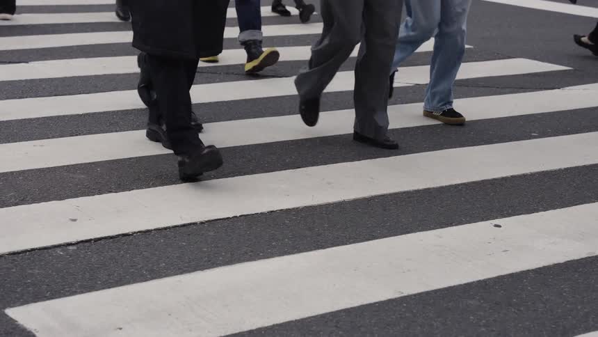 A slow-motion, low-angle shot of a crowd of anonymous pedestrians walking across a city crosswalk