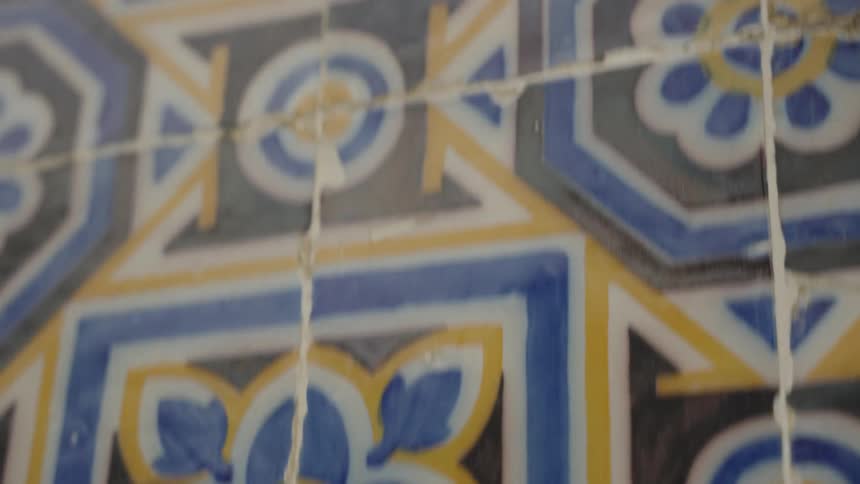 A slow tilt-up shot reveals an old wall of ornate and weathered blue, yellow, and black ceramic tiles