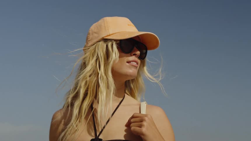 Slow motion close-up of a smiling blonde woman in a cap and sunglasses on a sunny day