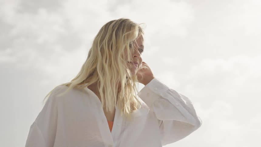 Slow motion shot of a serene young woman with blonde hair blowing in the wind on a bright, sunny day