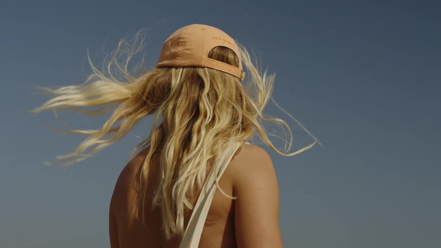 A blonde woman's hair blows in the wind in slow motion against a clear blue sky on a sunny day