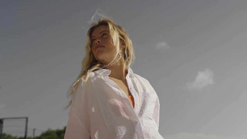 A beautiful blonde woman in a white beach cover-up enjoys the warm sun and gentle breeze in slow motion