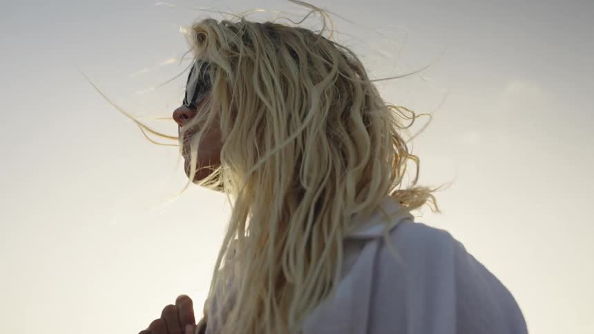 Slow motion shot of a beautiful blonde woman with windblown hair enjoying a peaceful walk along the ocean shore during a warm sunset
