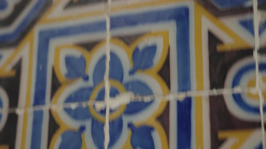 A detailed slow tilt-up shot reveals the intricate patterns and weathered cracks on a wall of traditional azulejo tiles