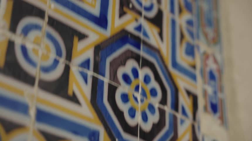 An extreme close-up shot with a shallow depth of field pans across a wall of intricate blue, yellow, and black patterned ceramic tiles