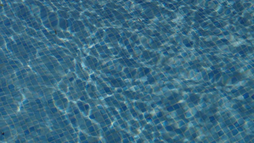 Glistening water ripples over blue mosaic tiles in a sunlit swimming pool