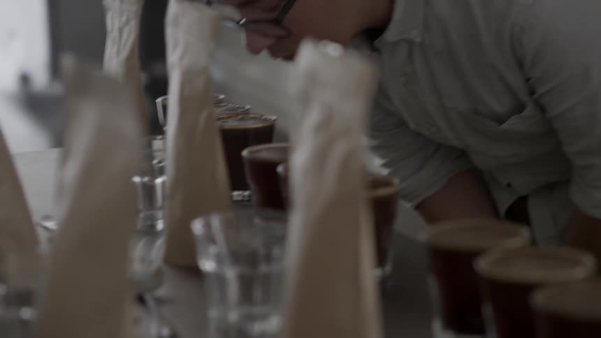A man bends over to smell the glasses filled with a brownish liquid
