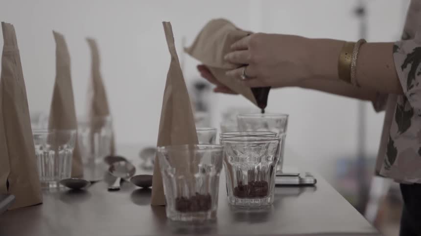 A woman pours coffee beans into glass cups